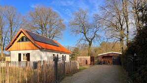 A wooden house with a sloped roof and a fenced driveway leading to a garage. - Ferienhaus, 90m², 1-8 Pers (Rheine)