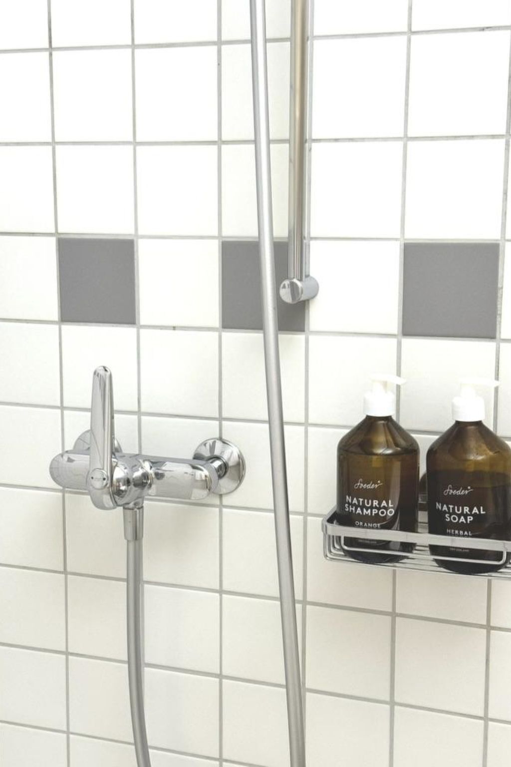 A shower area with a chrome faucet and a handheld showerhead. There are two bottles of 'Freder's Natural Shampoo' and 'Freder's Natural Soap' on a shelf.