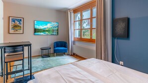 A bedroom with a bed, a desk, a chair, a TV, and a window with curtains. - Steil Alva Studios Smit by Interhome (Lenzerheide)