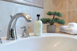 A bathroom sink with a modern faucet, a bottle of Pure Herbs, and a small potted plant. - Landhaus Ellerbrock (St. Peter-Ording)