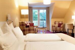 A hotel room with a bed, two armchairs, a small table, and a balcony with a view. - Landhaus Ellerbrock (St. Peter-Ording)