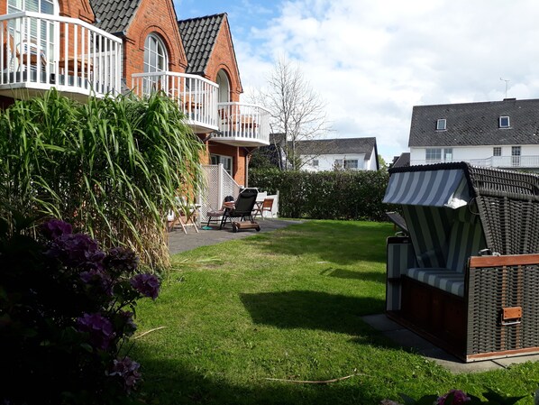 A residential property with a well-maintained lawn, outdoor seating area, and a large brick house with a balcony. - Landhaus Ellerbrock (St. Peter-Ording)