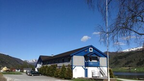 A building with a blue and white exterior, a covered entrance, and a view of a lake and mountains in the background. - VOSSESTØLEN HOTEL (Voss)