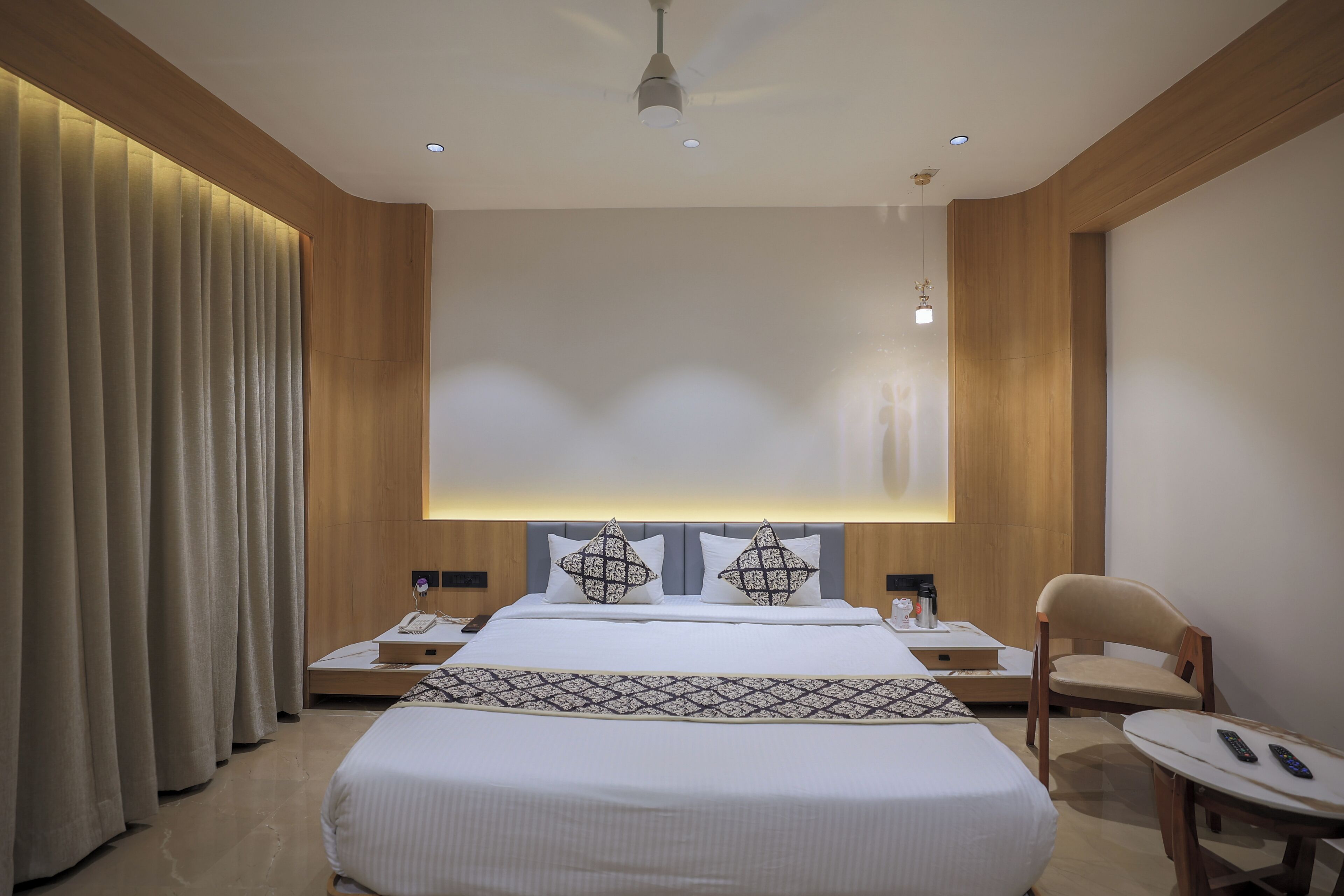 A modern hotel room with a large bed, two bedside tables, a chair, and a desk.