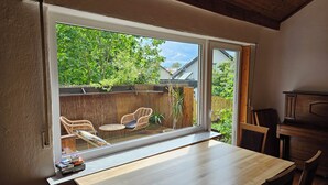 Une pièce dotée d’une grande porte-fenêtre coulissante donnant sur un jardin, d’une table en bois et de chaises en osier.