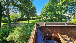 Une terrasse en bois dotée d’un espace salon intégré, entourée d’une végétation luxuriante et d’arbres.