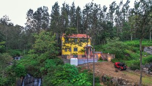 Un edificio amarillo con techo rojo, rodeado de un bosque denso y una cascada.