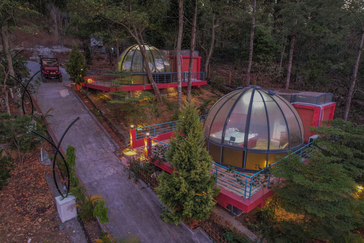 A forested area with dome-shaped structures, each with a small porch and seating area, connected by a paved path.