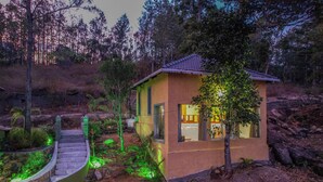 A small, single-story building with a tiled roof, surrounded by trees and a stone pathway leading to it. - Rain Rock Villa (Yercaud)