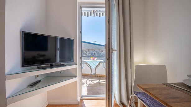 A modern room with a TV on a glass shelf, a wooden table, and a view of a balcony with a table and chairs. - Casa Lorenzo OG - Ap 2 - 1.kat (Premantura)