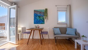A modern living room with a wooden floor, a gray sofa with blue cushions, a dining table with two chairs, and a large abstract painting on the wall. - Casa Lorenzo OG - Ap 2 - 1.kat (Premantura)