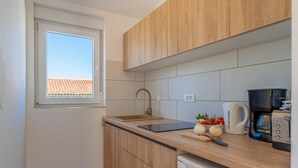 A compact kitchen with a window, wooden cabinets, a sink, a coffee maker, and a toaster. - Casa Lorenzo OG - Ap 2 - 1.kat (Premantura)