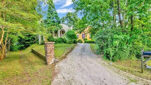 A residential street with a stone pillar, a house with a porch, and lush greenery. - Historic Spanish Charm + Scenic View | Cozy Casita (Birmingham)
