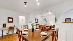 A dining area with a wooden table set for four, surrounded by chairs. There is a sofa and a lamp in the background. - Historic Spanish Charm + Scenic View | Cozy Casita (Birmingham)