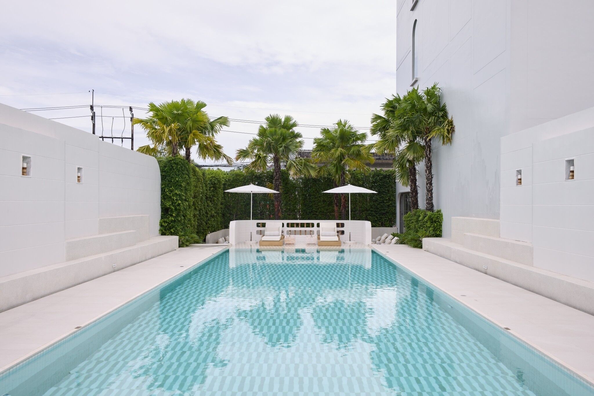 A rectangular swimming pool with checkered tiles, surrounded by white walls and palm trees.