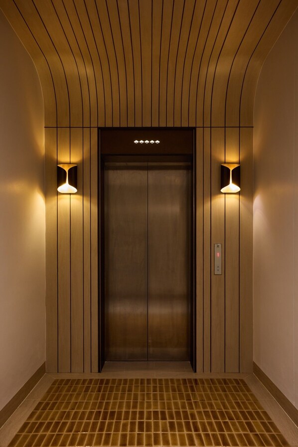 An elevator with a wooden panel design, two wall-mounted lights, and a control panel. - Arco Phuket Town (Phuket)