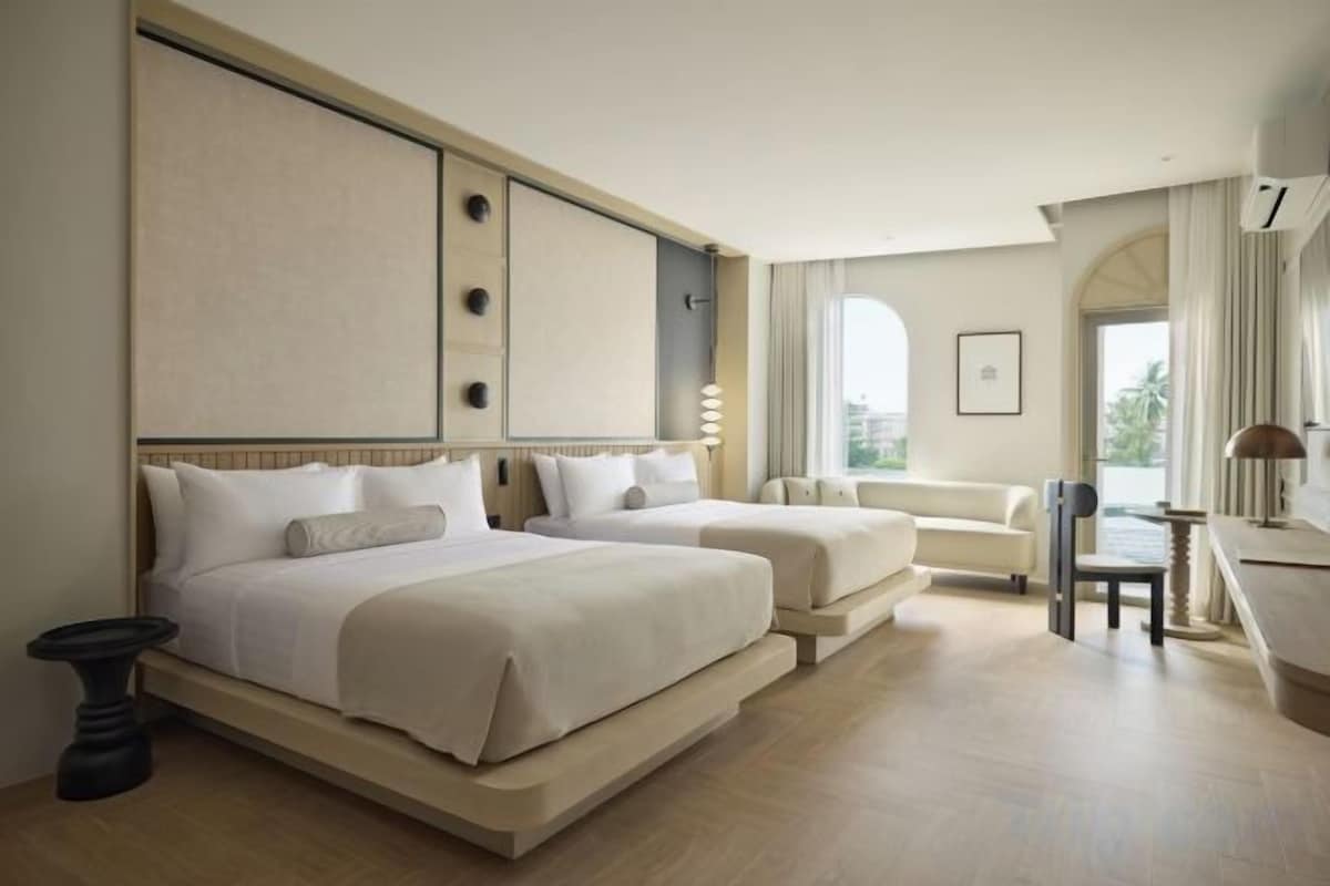 A hotel room with two beds, a sofa, a desk, and a view of the outdoors.