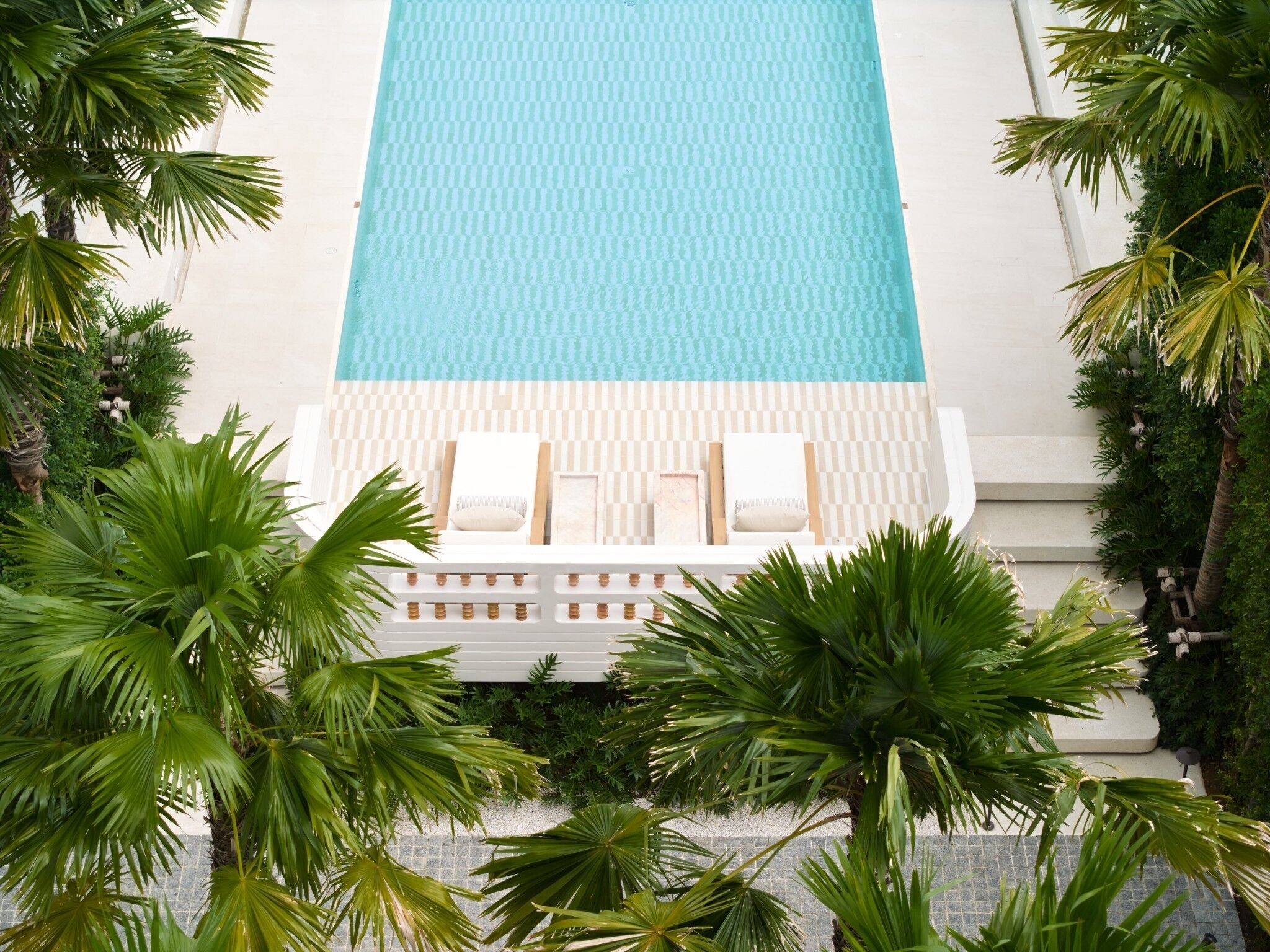 A pool with two lounge chairs and a small table, surrounded by palm trees.
