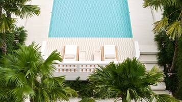 A pool with two lounge chairs and a small table, surrounded by palm trees.