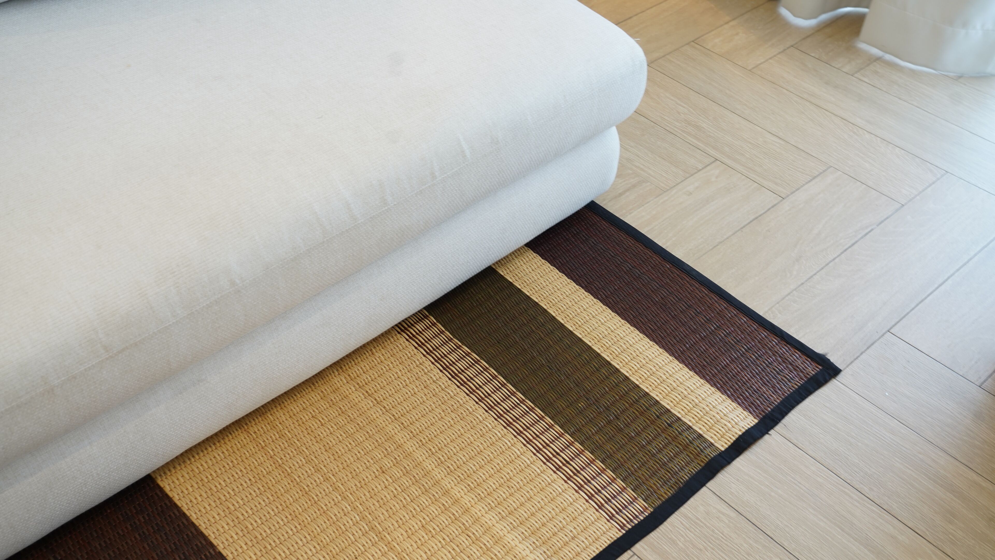 A section of a room with a beige sofa and a striped area rug on a wooden floor.