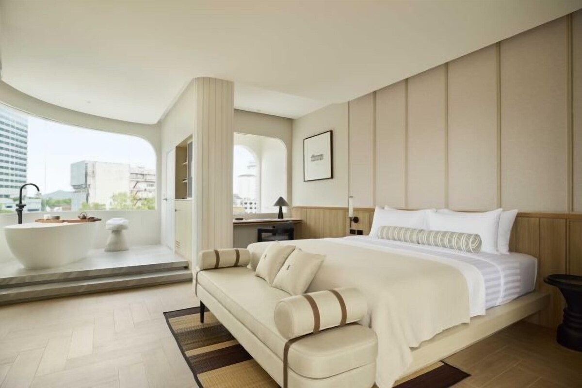 A modern hotel room with a large bed, a sofa, a bathtub, and a view of the city.