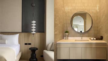 A modern hotel room with a bed, bedside table, and a large mirror above the vanity.
