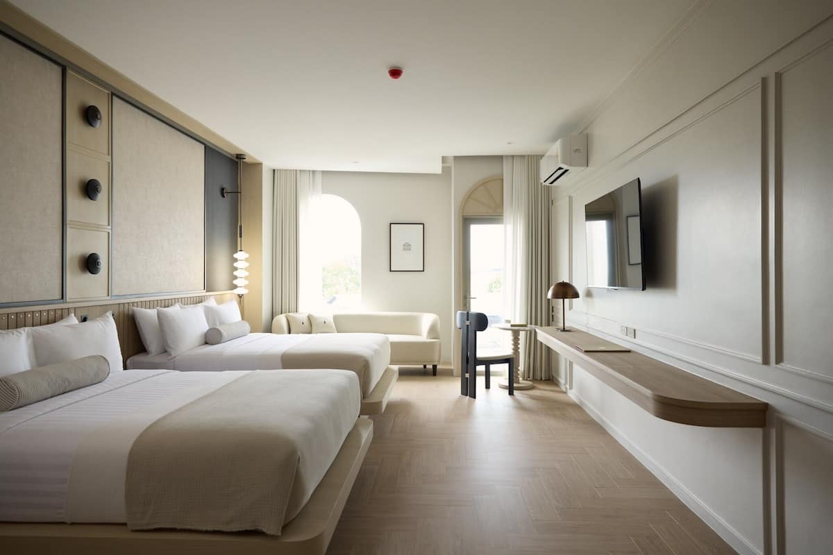 Une chambre d’hôtel avec deux lits, un bureau, une chaise, une télévision et une fenêtre avec des rideaux.