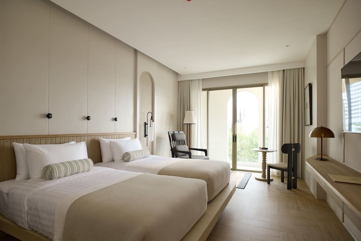 Une chambre d’hôtel avec deux lits, un bureau, une chaise et une vue sur l’extérieur.