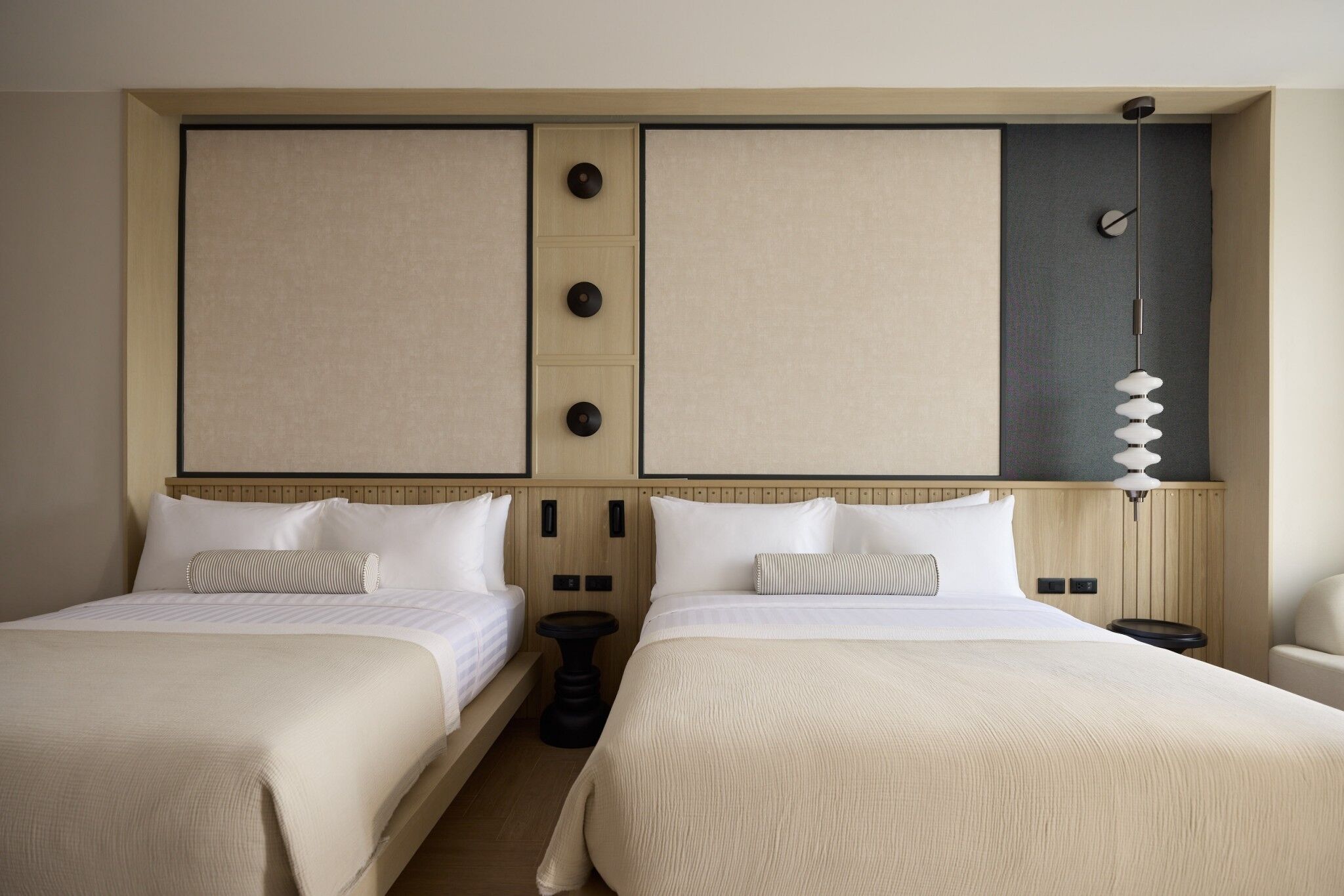 A double room with two beds, a small table, and a wall-mounted lamp.