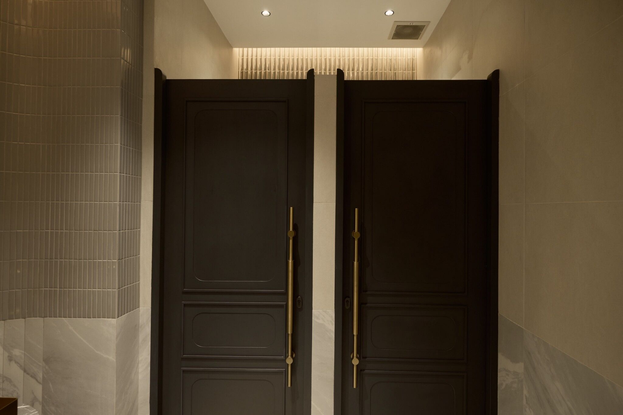 A dark wooden door with a gold handle in a hallway with tiled walls.