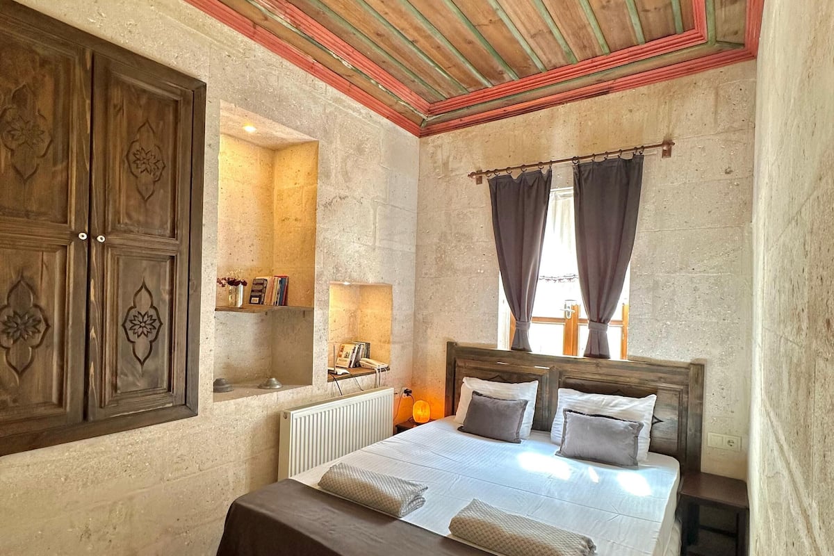 A bedroom with a wooden bed, a nightstand, a dresser, and a window with curtains.