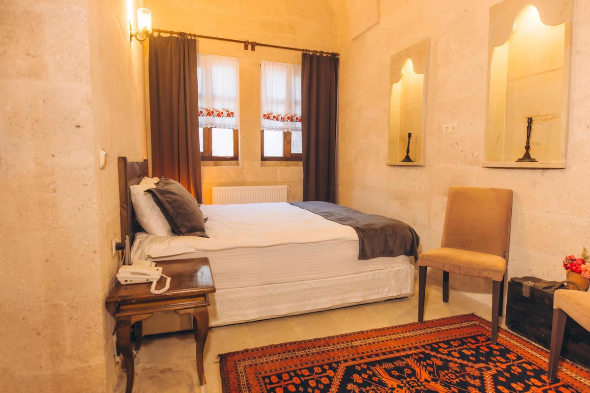 A bedroom with a bed, a chair, a nightstand, a lamp, and a mirror.