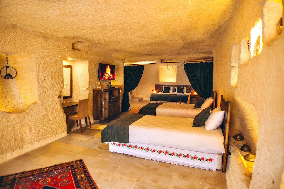 A cozy, rustic bedroom with a large bed, a desk with a chair, and a television displaying a fire.