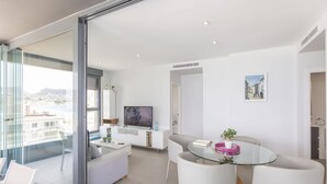 A modern living room with a glass dining table, white sofas, and a TV. - Apartamento Infinium 3 - Costa CarpeDiem (Calpe)