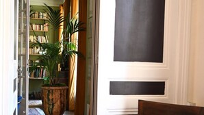 A wooden chair with a blue cushion in a hallway with a fireplace, a bookshelf, and a potted plant. - Olympic Games 2024 : Direct to Stade de France (Paris)