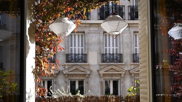 An outdoor seating area with a table and chairs, a bamboo fence, and a building with balconies in the background. - Olympic Games 2024 : Direct to Stade de France (Paris)