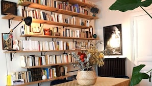 A cozy reading nook with a wooden bookshelf filled with books, a table with a patterned tablecloth, and blue chairs. - Olympic Games 2024 : Direct to Stade de France (Paris)