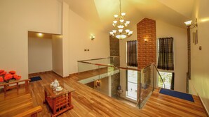 A spacious loft with a wooden floor, a glass railing, a chandelier, and a brick accent wall. - Rock Villa  (Ootacamund)