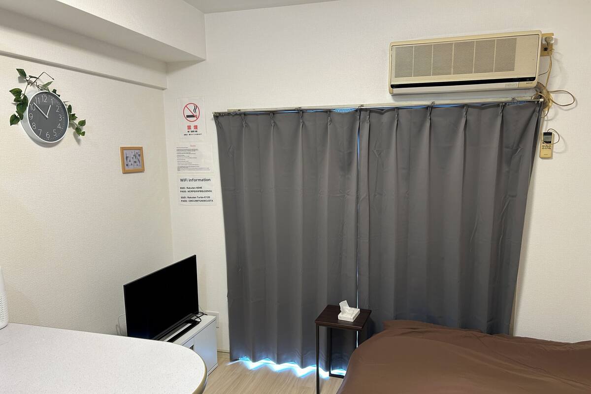 A hotel room with a bed, a desk, a chair, a TV, an air conditioner, and a curtain.