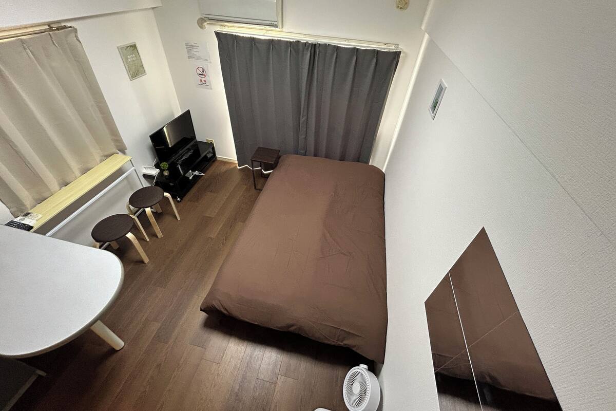 A compact hotel room with a single bed, a small desk with a chair, a television, and a window with curtains.