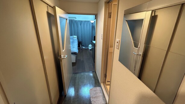 Un couloir étroit au plancher en bois, un tapis blanc et un lit avec un rideau bleu en arrière-plan.