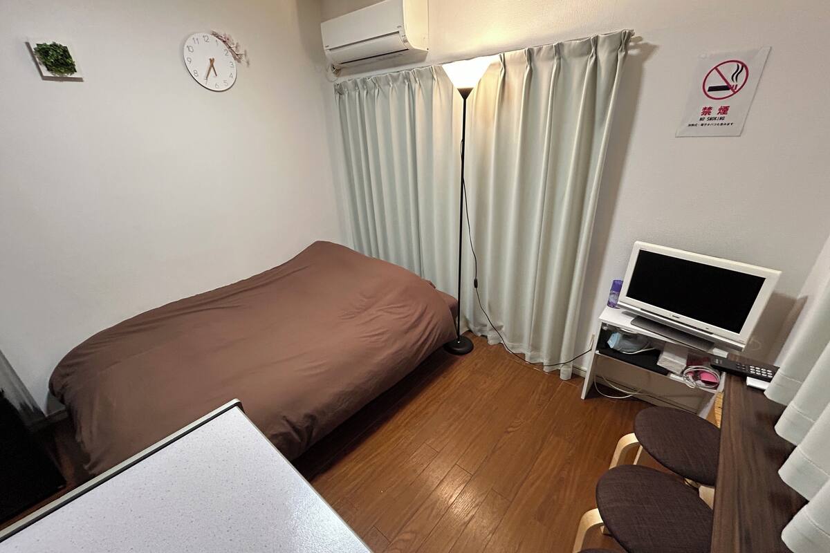 A hotel room with a bed, a desk with a computer, a TV, and a chair.