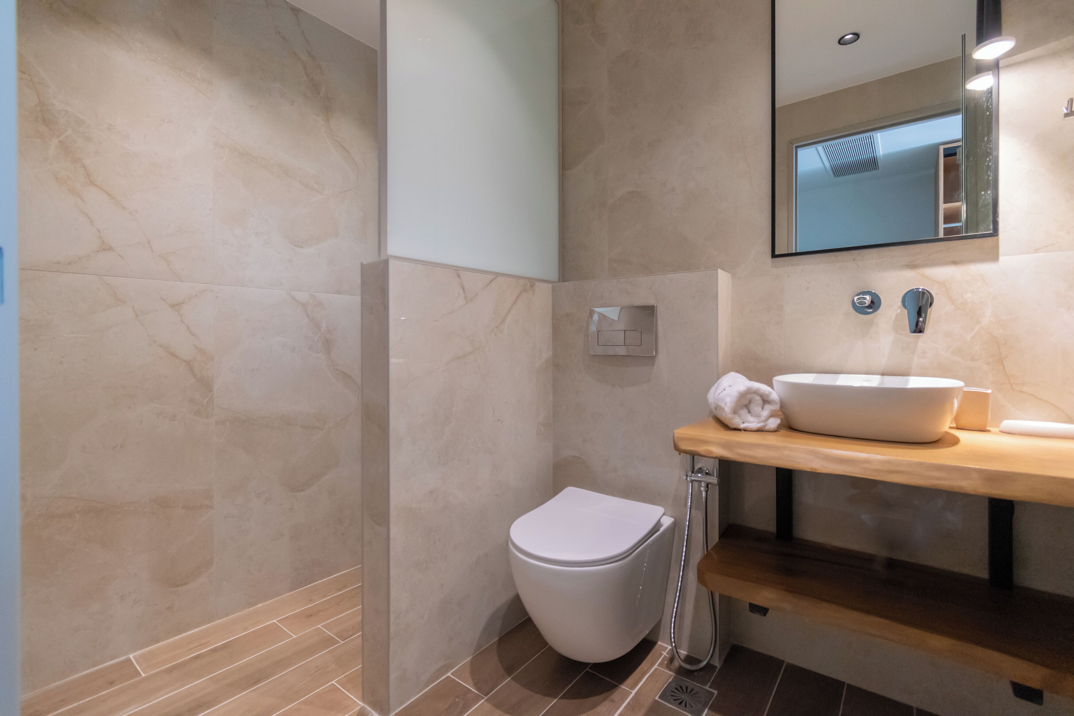 A modern bathroom with a marble wall, a white toilet, a wooden vanity with a sink, and a mirror.
