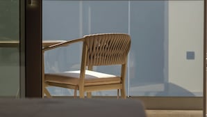 Una silla con respaldo y asiento tejido, ubicada en un balcón con pared de vidrio.