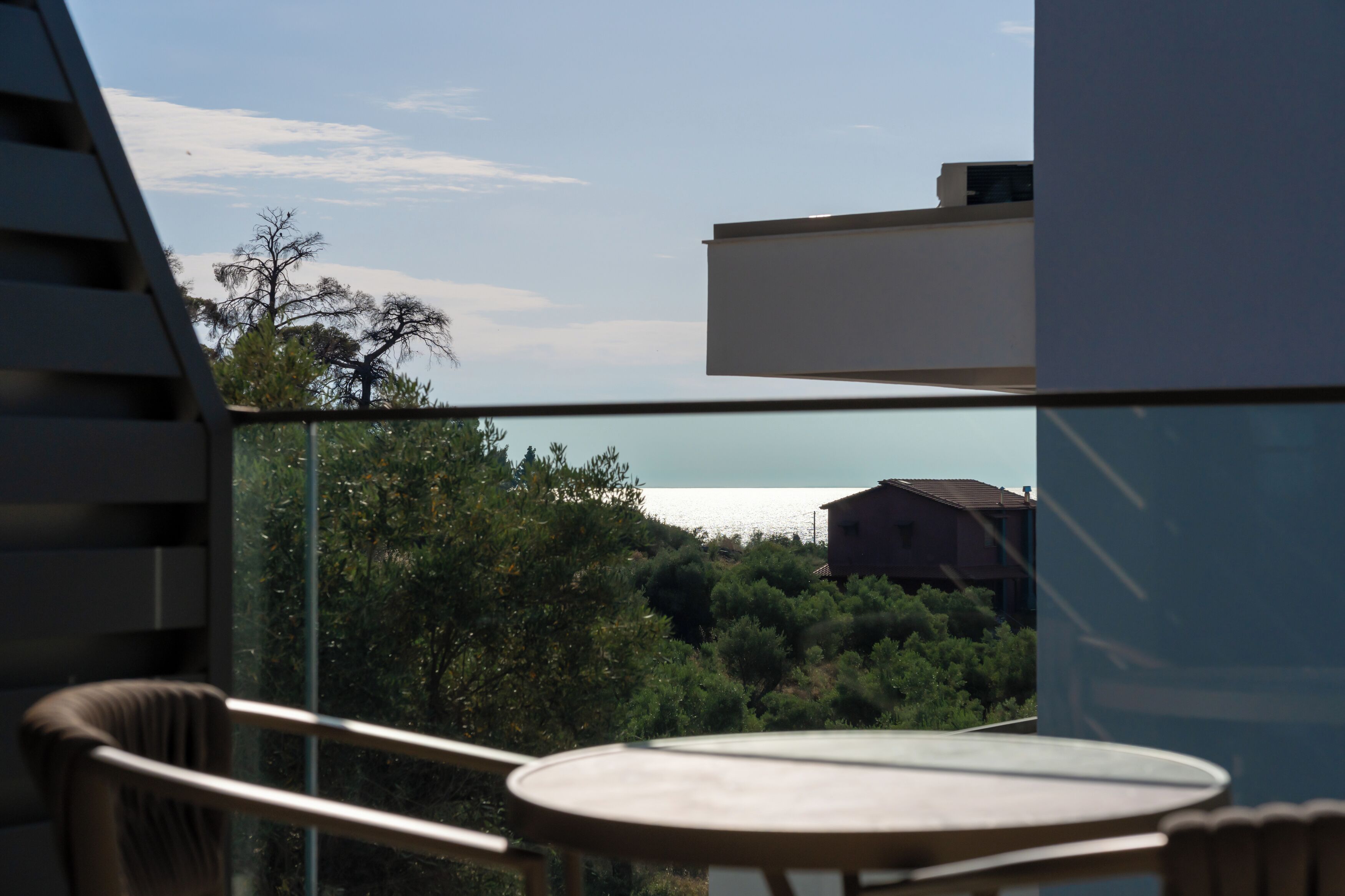A balcony with a table and chairs, overlooking a landscape with trees and a building in the distance.