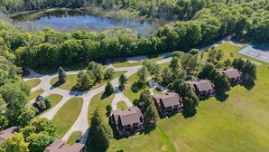 An aerial view of a residential area with multiple houses, a pond, and a tennis court. - The Rushes (Baileys Harbor)