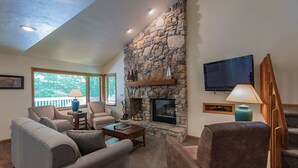 A living room with a stone fireplace, a television, and a staircase. - The Rushes (Baileys Harbor)