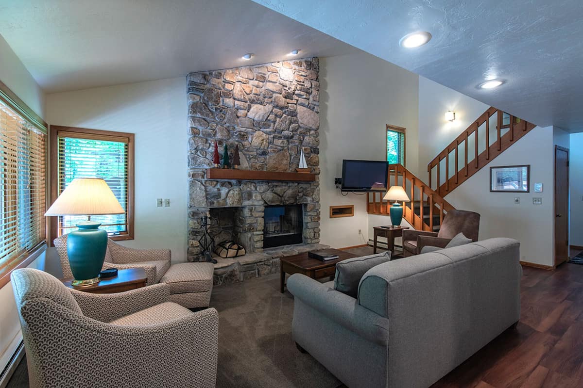 A living room with a stone fireplace, a television, and a staircase.