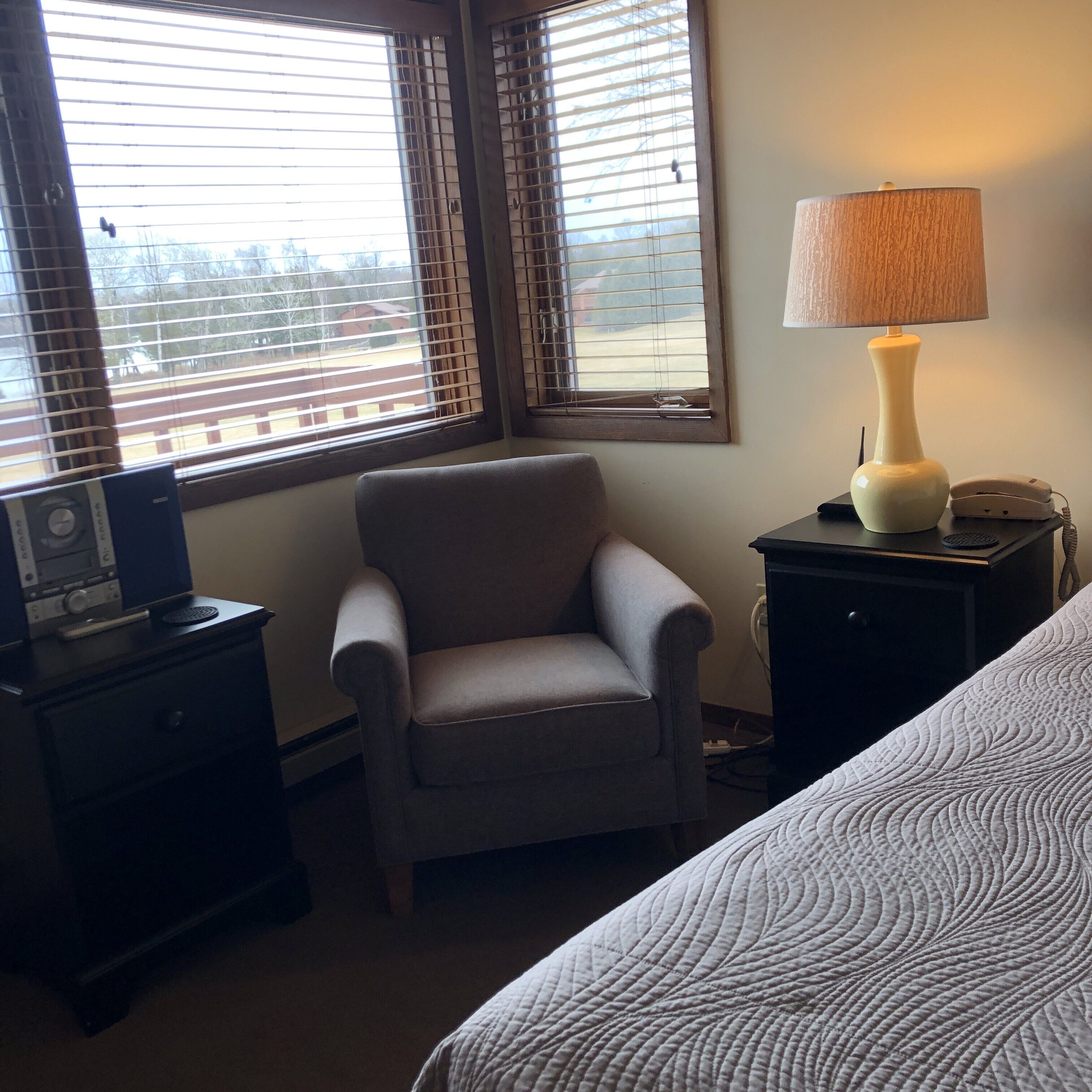 A bedroom with a single armchair, a bedside table with a lamp, and a bed with a quilted cover.