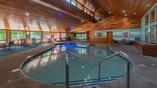 An indoor swimming pool with wooden ceiling beams, clear glass walls, and a tiled floor. - The Rushes (Baileys Harbor)